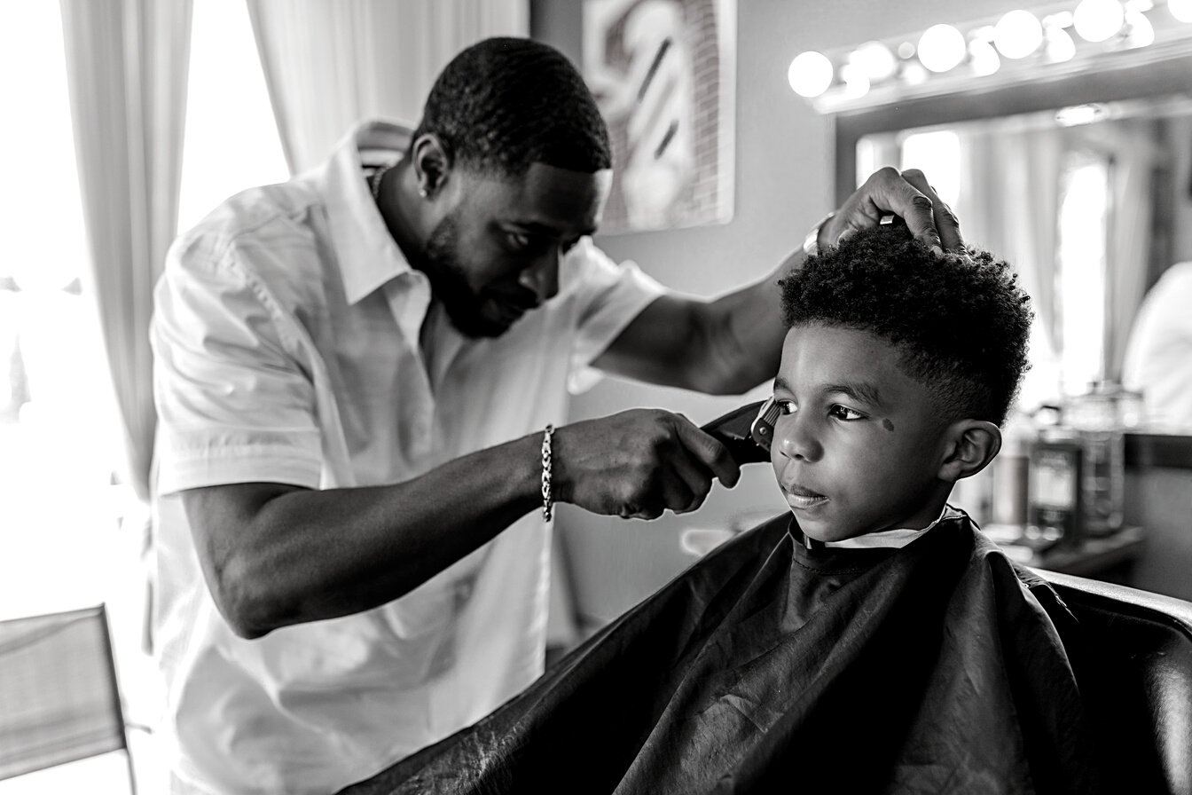 A Barber Holding a Hair Clipper Trimming a Boy's Hair